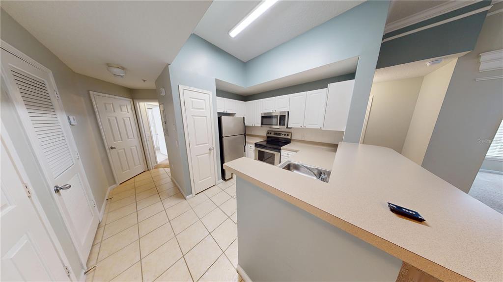 A kitchen features white cabinets, stainless steel appliances, and a breakfast bar with beige countertops — 235 GOLDENRAIN DRIVE UNIT 303, CELEBRATION, FL