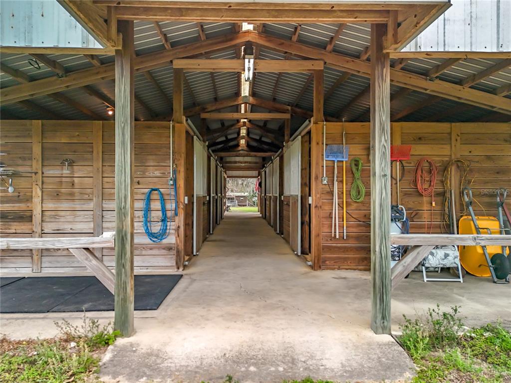 A covered outdoor aisle leads between two rows of wooden horse stalls with concrete flooring — 41204 EMERALDA ISLAND ROAD, LEESBURG, FL