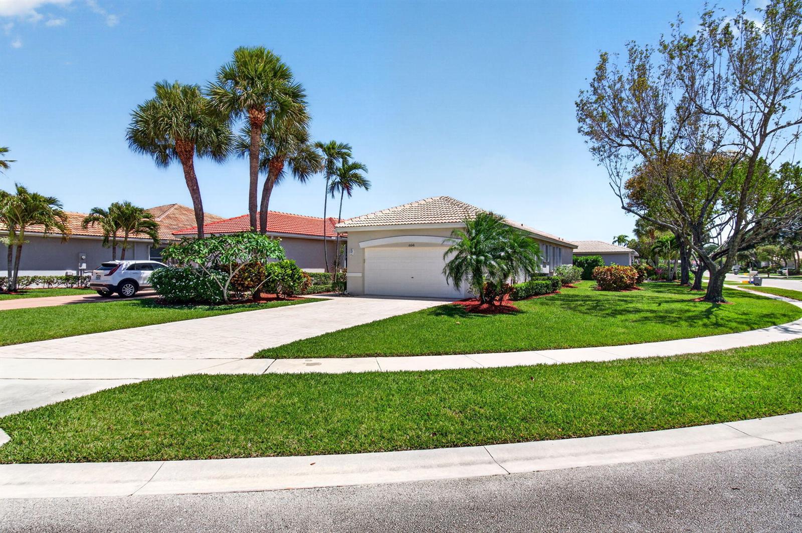 A single-story house with a white garage, palm trees, and a green lawn under blue sky — 10641 Royal Caribbean Circle, Boynton Beach FL 33437, BOYNTON BEACH, FL