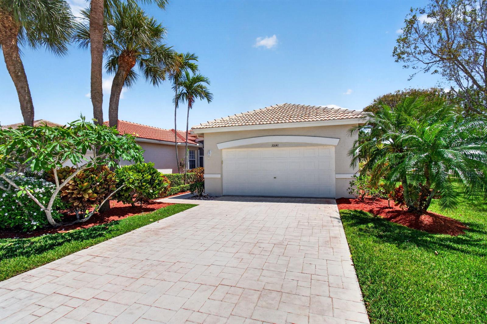 A paved driveway leads to the garage of a single-story home with palm trees — 10641 Royal Caribbean Circle, Boynton Beach FL 33437, BOYNTON BEACH, FL