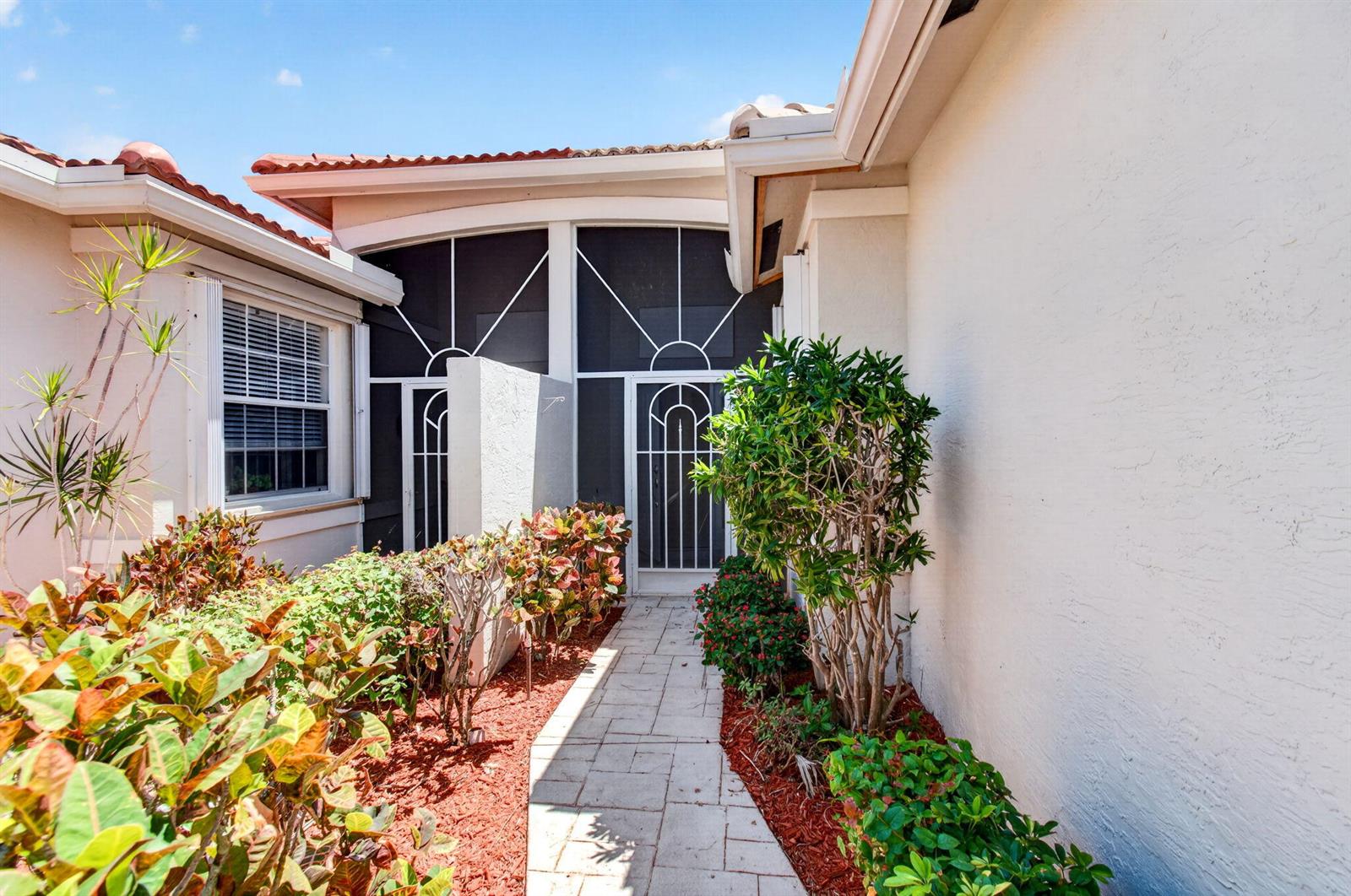 A stone walkway leads to a screened-in entryway surrounded by landscaping and stucco walls — 10641 Royal Caribbean Circle, Boynton Beach FL 33437, BOYNTON BEACH, FL