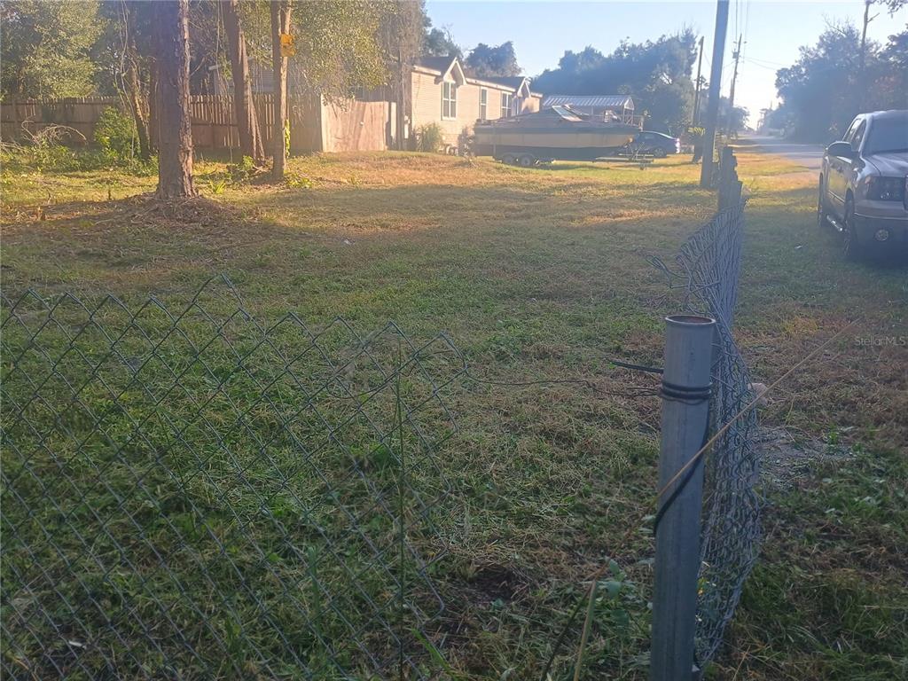 A grassy, fenced-in vacant lot with a boat and a house in the background — 27847 VEVA AVENUE, PAISLEY, FL