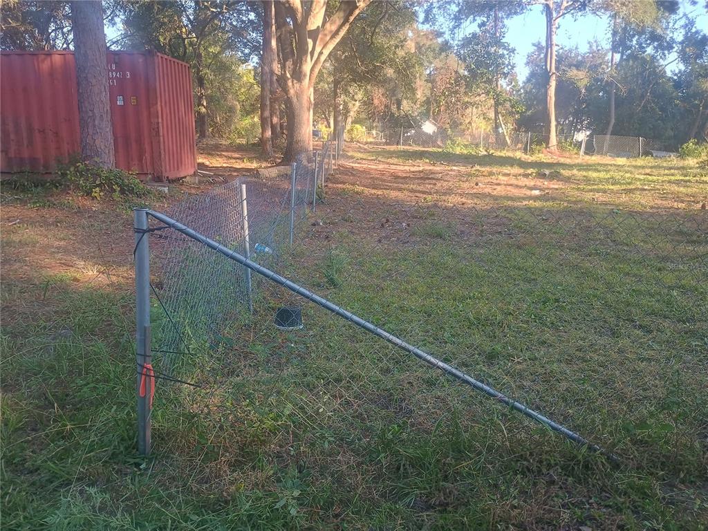 A chain-link fence runs through a grassy yard next to a red shipping container — 27847 VEVA AVENUE, PAISLEY, FL