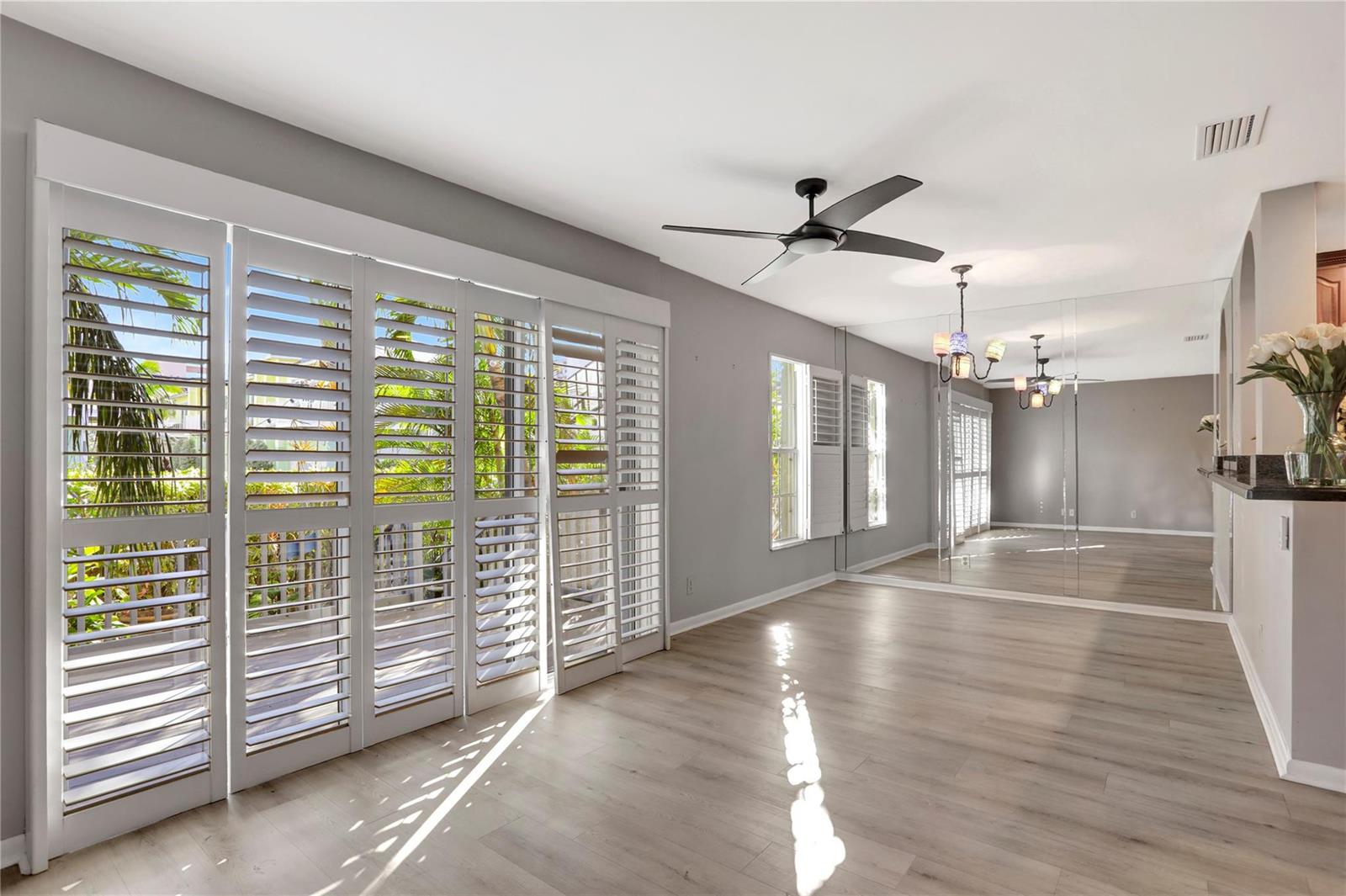 A bright dining room features light wood flooring, plantation shutters, a ceiling fan, and mirrored walls — 3213 NE 16th Street # 112, Pompano Beach FL 33062, POMPANO BEACH, FL