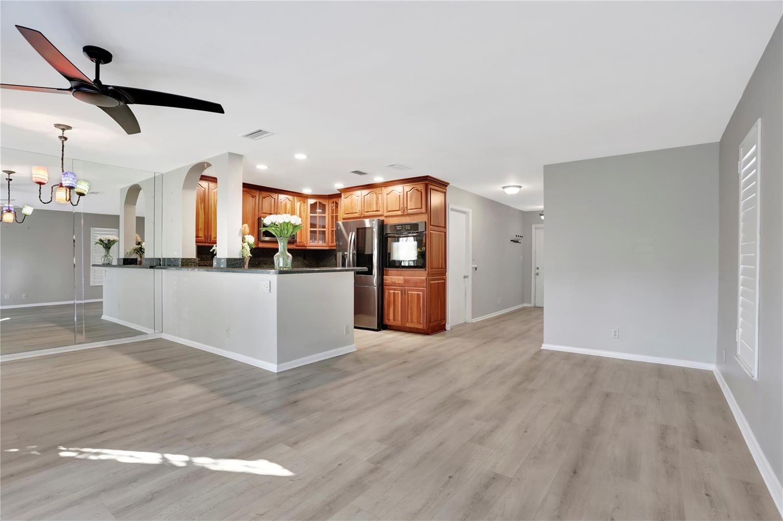 A kitchen with wood cabinets and stainless steel appliances opens to a light-floored living area — 3213 NE 16th Street # 112, Pompano Beach FL 33062, POMPANO BEACH, FL