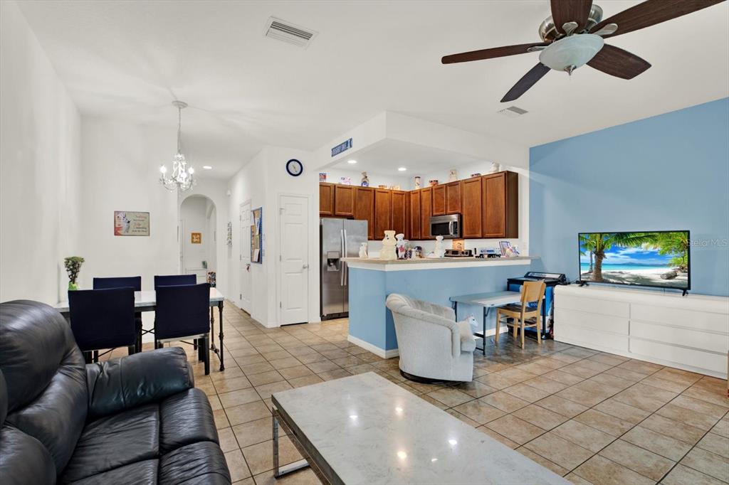 An open-concept living and dining area features tile flooring, a kitchen with wood cabinets, and a television — 6843 46TH LANE N, PINELLAS PARK, FL