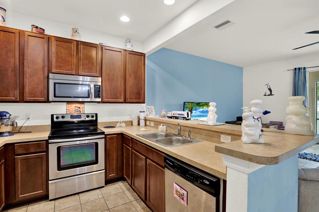 A kitchen features wood cabinets, stainless steel appliances, and a breakfast bar overlooking a room — 6843 46TH LANE N, PINELLAS PARK, FL