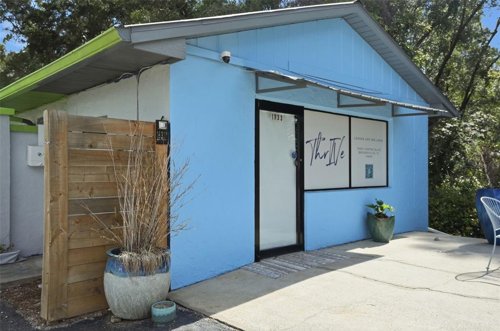 A light blue building exterior features a glass door, a wooden privacy screen, and planters — 16331 CORTEZ BOULEVARD, BROOKSVILLE, FL