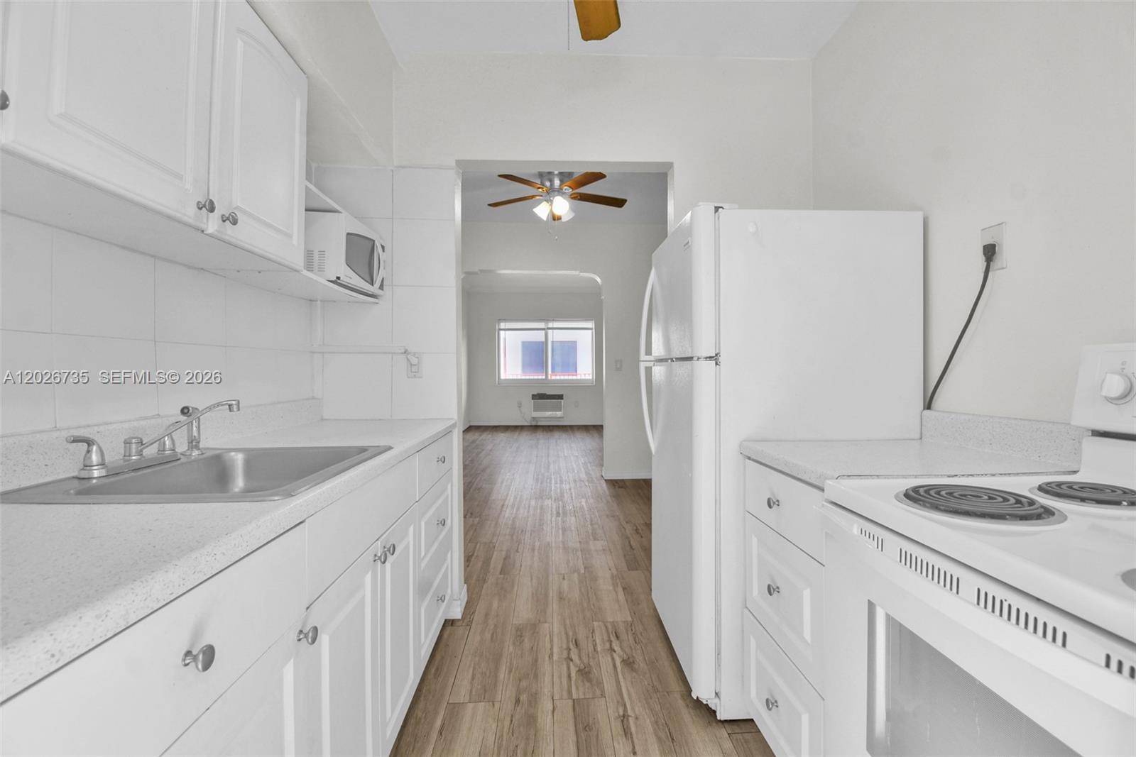 A galley kitchen features white cabinets, white appliances, and light wood-look flooring — 1135 Euclid Ave # 202, Miami Beach FL 33139, MIAMI BEACH, FL