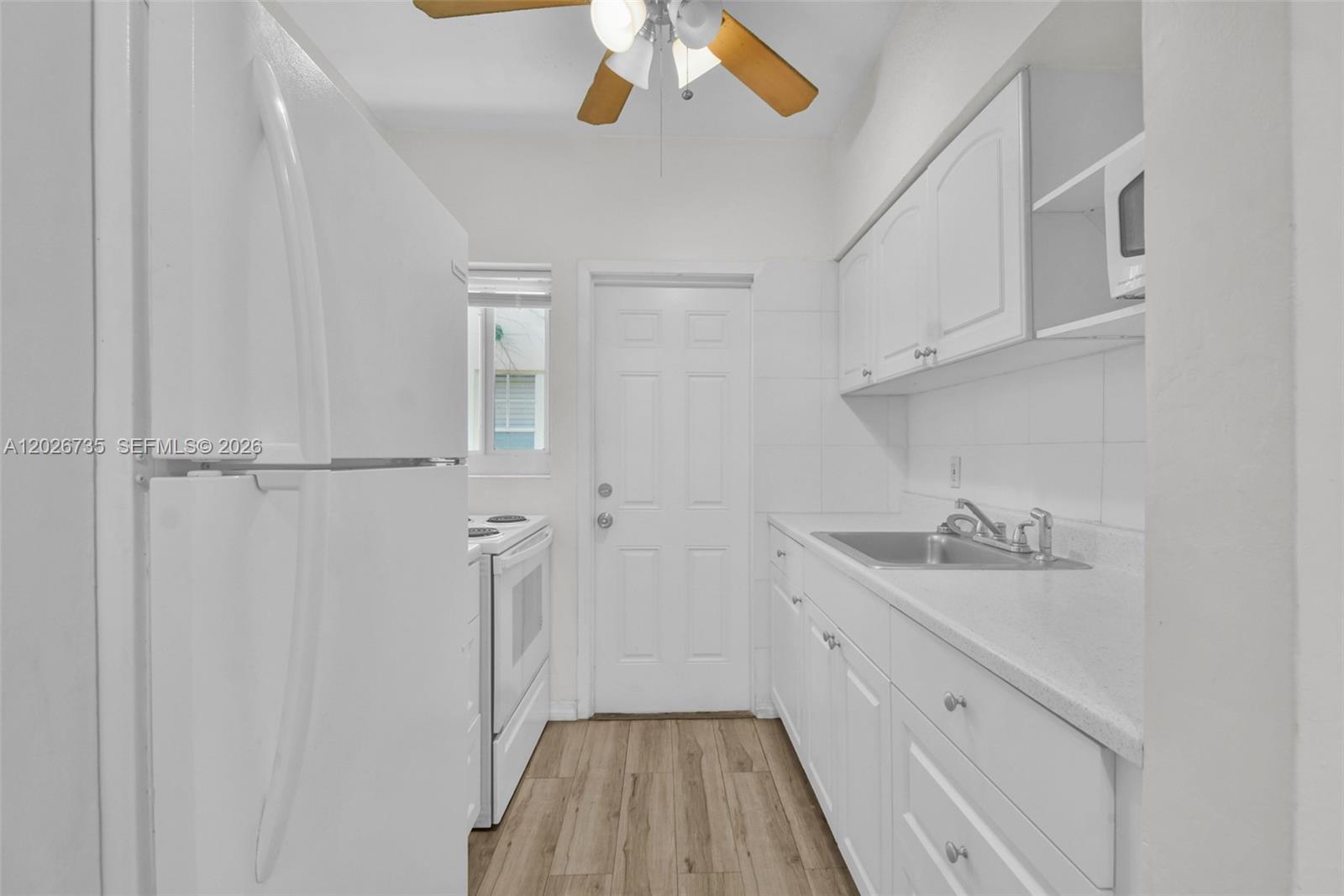 A galley-style kitchen features white cabinets, a stainless steel sink, and light wood-look flooring — 1135 Euclid Ave # 202, Miami Beach FL 33139, MIAMI BEACH, FL