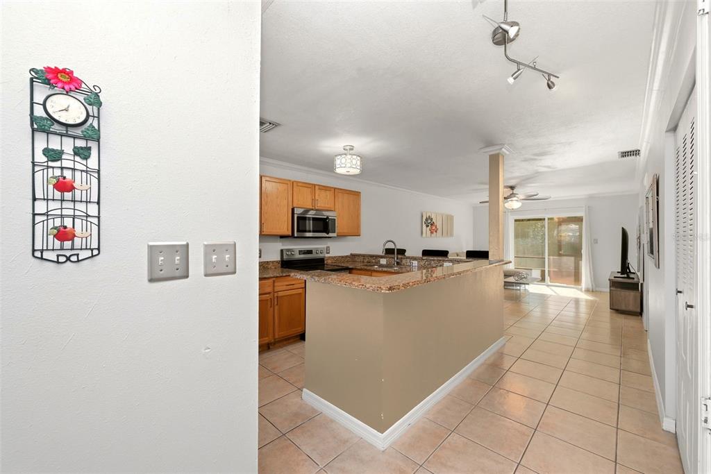 A kitchen with wood cabinets and granite countertops opens to a living area with tile floors — 4410 BAR HARBOR DRIVE, ORLANDO, FL