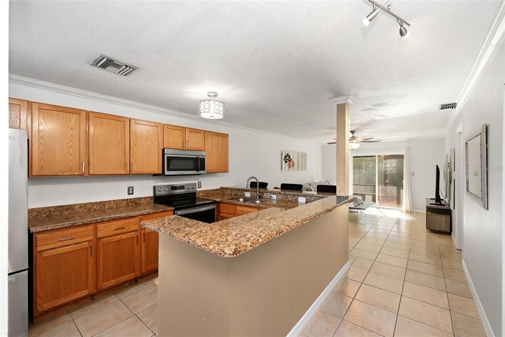 A kitchen with wood cabinets, granite countertops, and tile flooring opens to a living area — 4410 BAR HARBOR DRIVE, ORLANDO, FL