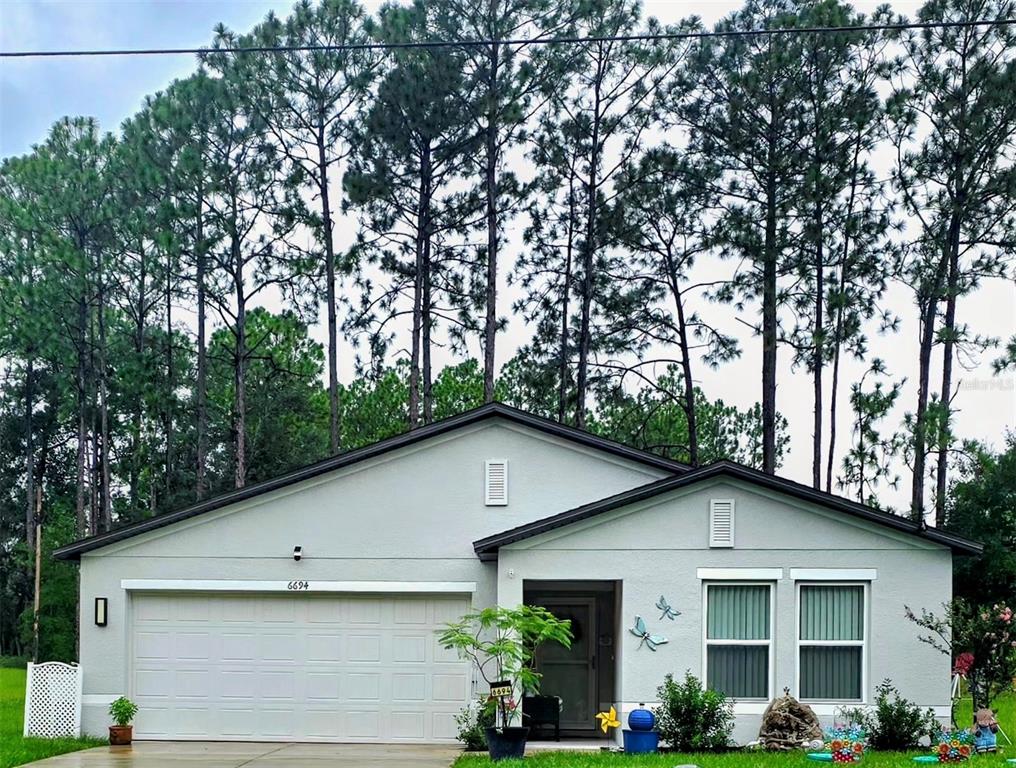 A single-story house with a two-car garage and light gray stucco exterior sits among trees — 6694 N EDELWEISS WAY, CITRUS SPRINGS, FL