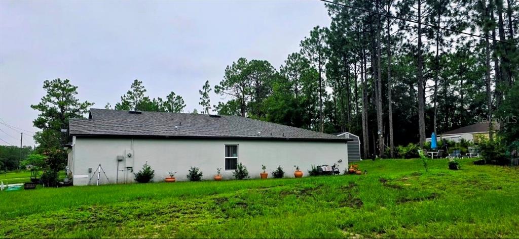 The exterior side view of a light-colored house features a single window and grassy yard — 6694 N EDELWEISS WAY, CITRUS SPRINGS, FL