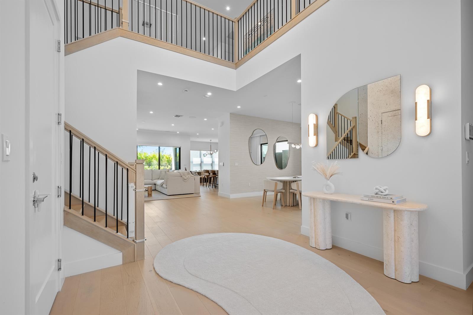 A bright foyer features light wood flooring, a curved rug, a console table, and stairs — 20135 Casa De Campo Lane, Boca Raton FL 33434, BOCA RATON, FL