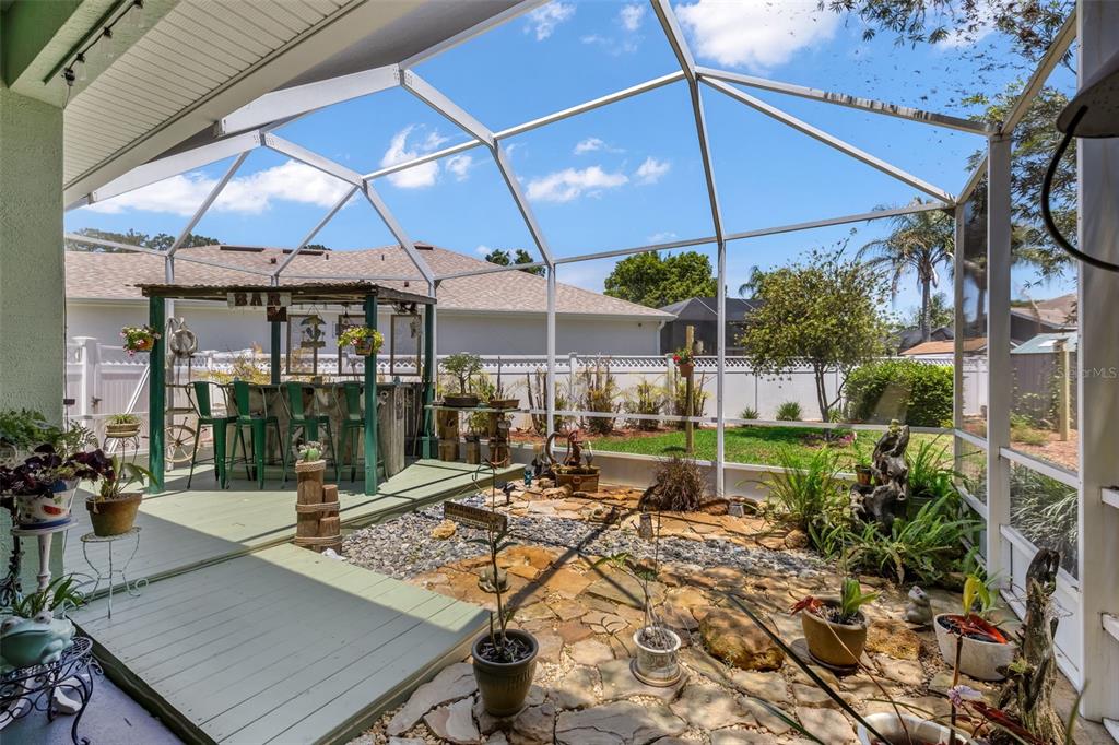 A screened-in patio features a wooden bar, stone flooring, and various potted plants — 54 EDITH POPE DRIVE, PALM COAST, FL