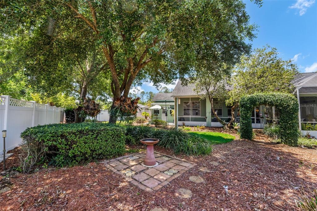 A backyard features a birdbath on a brick patio, mature trees, and a screened porch — 54 EDITH POPE DRIVE, PALM COAST, FL