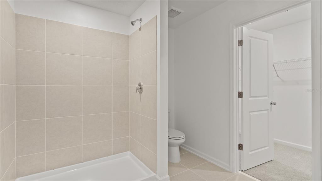 A tiled shower stall sits next to a toilet and an open walk-in closet door — 6280 BOTTICELLA BOULEVARD, WINTER HAVEN, FL