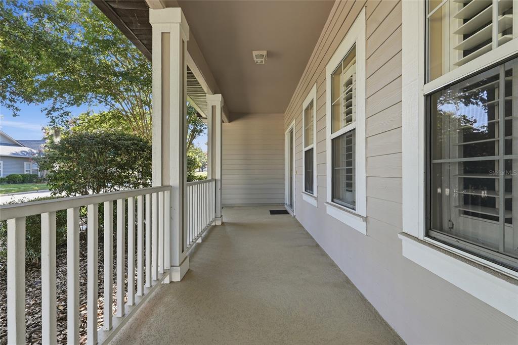 A covered porch with white railings, beige siding, and multiple windows along the exterior wall — 8693 SW 76TH PLACE, GAINESVILLE, FL