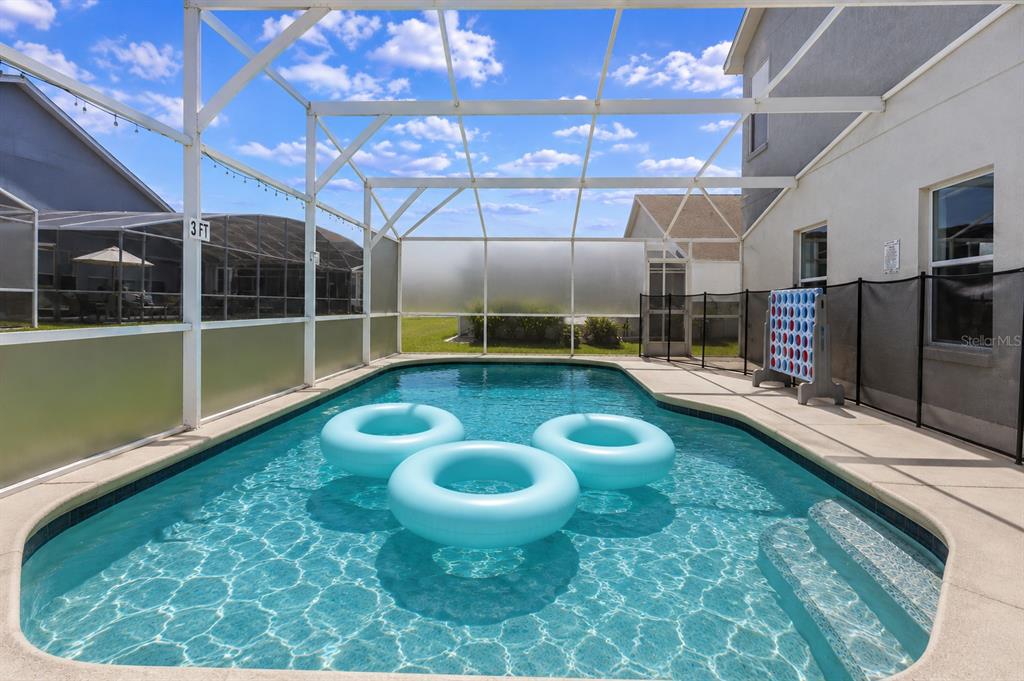 A screened-in swimming pool with three blue inflatable rings sits behind a residential home — 186 NAZHA DRIVE, DAVENPORT, FL