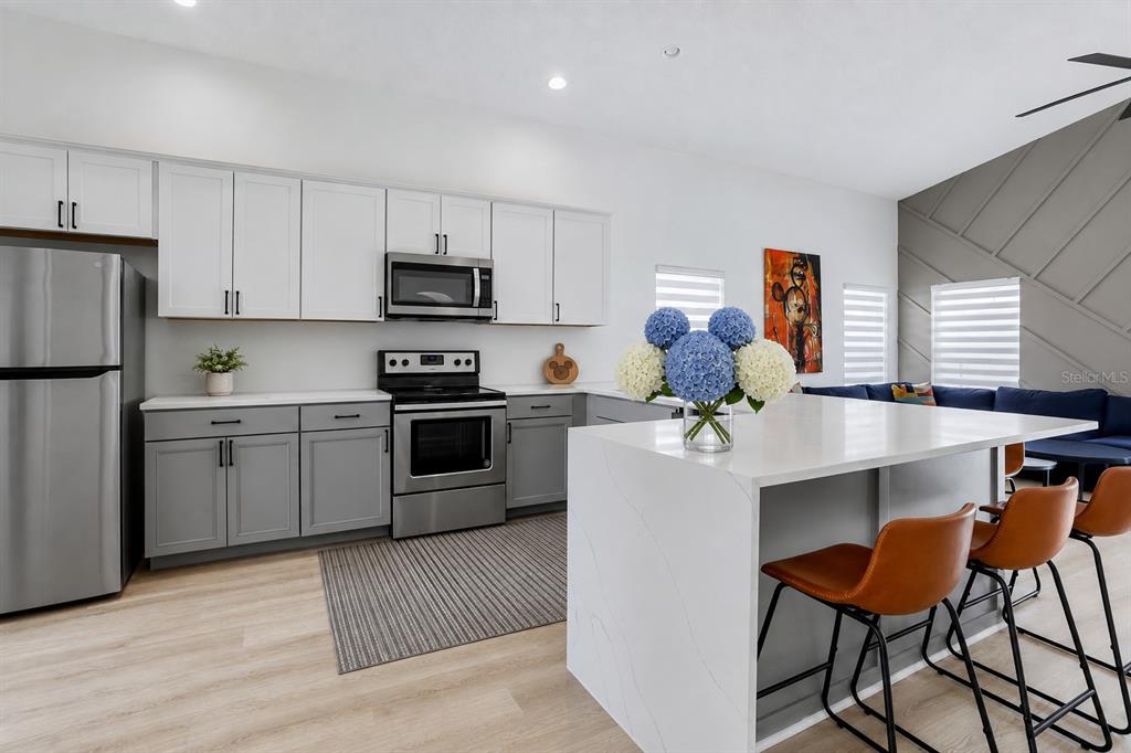 A modern kitchen features white upper cabinets, gray lower cabinets, stainless steel appliances, and a quartz-topped island — 186 NAZHA DRIVE, DAVENPORT, FL