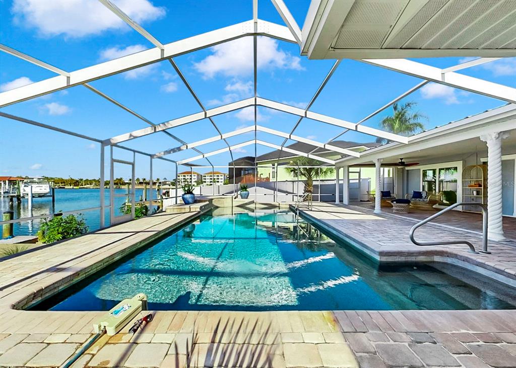 A screened-in swimming pool overlooks a canal with a dock and distant buildings — 6344 COTTONWOOD LANE, APOLLO BEACH, FL