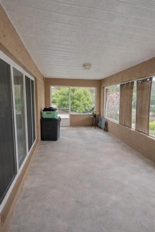 A covered, enclosed porch features concrete flooring, beige stucco walls, and large windows — 549 WHITE PLAINS AVENUE SW, PALM BAY, FL