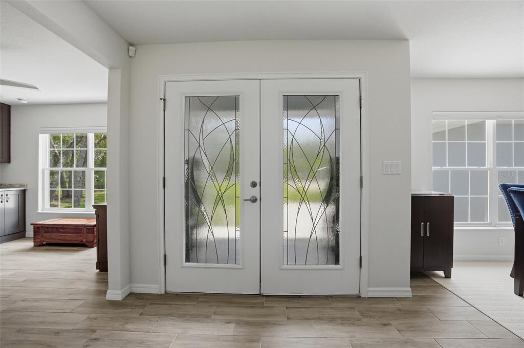 A bright entryway features double glass-paneled doors, light-colored walls, and wood-look tile flooring — 10345 MEADOW WREN AVENUE, WEEKI WACHEE, FL