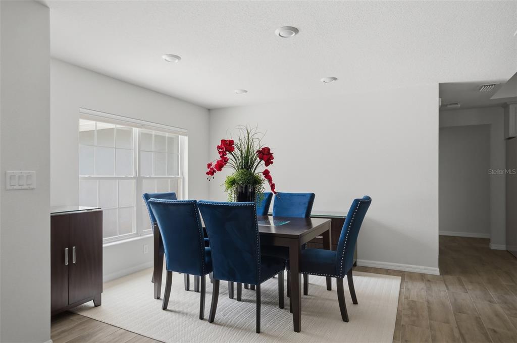 A dining room features a dark wood table, six blue upholstered chairs, and a floral centerpiece — 10345 MEADOW WREN AVENUE, WEEKI WACHEE, FL