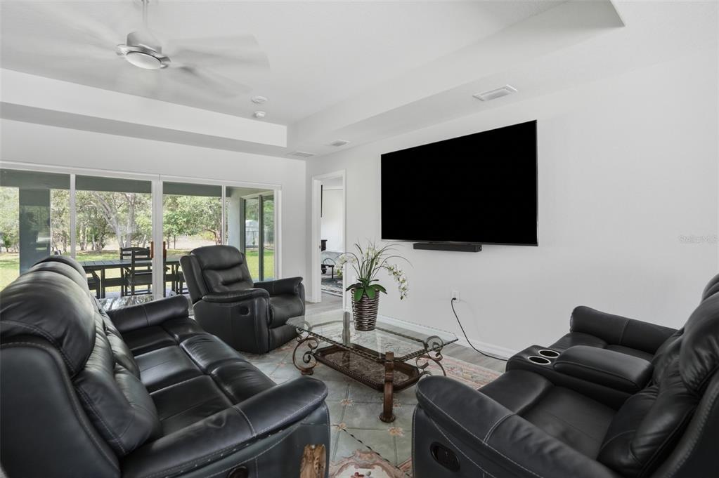 A living room features black leather furniture, a wall-mounted television, and sliding glass patio doors — 10345 MEADOW WREN AVENUE, WEEKI WACHEE, FL