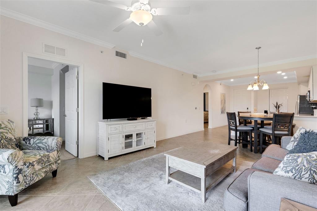 A living room with tile floors, a ceiling fan, a television, and a dining area — 17510 GAWTHROP DRIVE UNIT 204, BRADENTON, FL