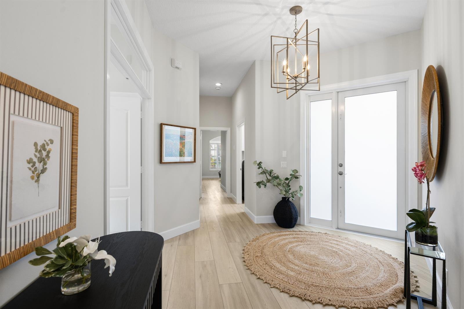 A bright entryway features light wood flooring, a geometric chandelier, and a round jute rug — 1009 Diamond Head Way, Palm Beach Gardens FL 33418, PALM BEACH GARDENS, FL
