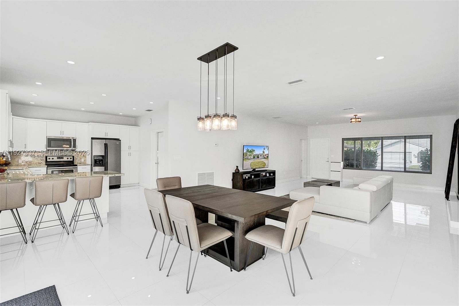An open-concept living and dining area features white tile floors, white cabinetry, and modern furniture — 1102 Meadowlark Ave, Miami Springs FL 33166, MIAMI SPRINGS, FL