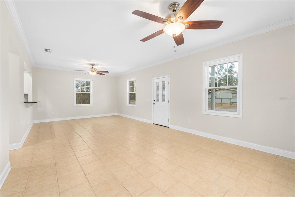 An empty living room features beige tile flooring, two ceiling fans, and white walls — 23187 NW 179 PLACE, HIGH SPRINGS, FL