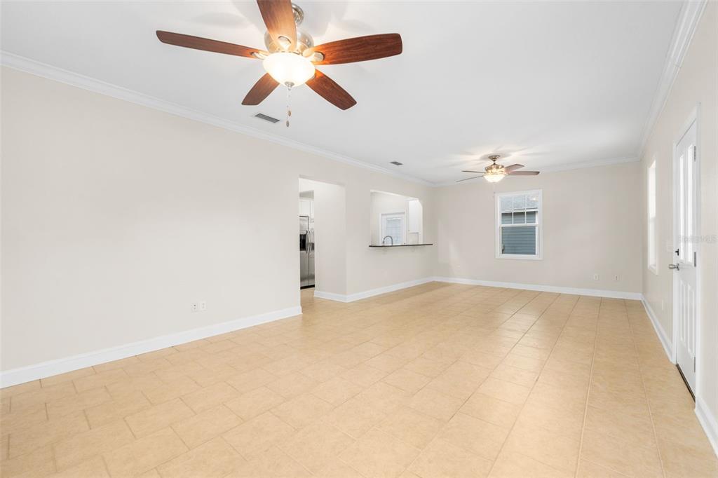 A spacious room with light-colored tile flooring, two ceiling fans, and a kitchen pass-through window — 23187 NW 179 PLACE, HIGH SPRINGS, FL