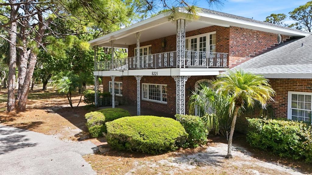 A two-story brick house features a full-length upper balcony with decorative white metal railings — 8221 DESOTO MEMORIAL HIGHWAY, BRADENTON, FL