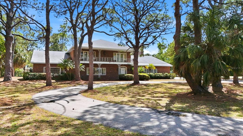 A two-story brick house with a balcony and a curved driveway sits among many trees — 8221 DESOTO MEMORIAL HIGHWAY, BRADENTON, FL
