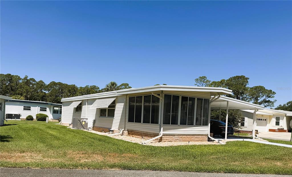 A single-story manufactured home features a screened-in porch, a carport, and light-colored siding — 111 CHESTNUT STREET, LEESBURG, FL