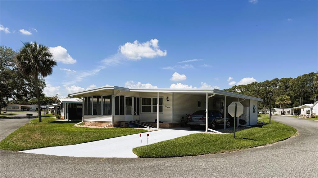 A single-story manufactured home with a carport, screened porch, and driveway sits on a corner lot — 111 CHESTNUT STREET, LEESBURG, FL