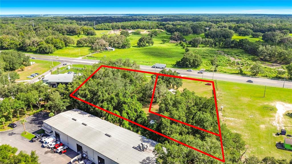 An aerial view shows two adjacent wooded lots outlined in red next to a commercial building — 1450 STATE ROAD 44, LEESBURG, FL