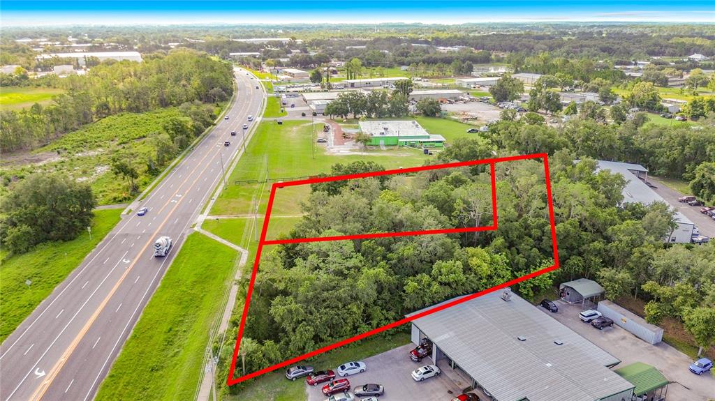An aerial view shows a wooded, trapezoidal plot of land outlined in red beside a highway — 1450 STATE ROAD 44, LEESBURG, FL