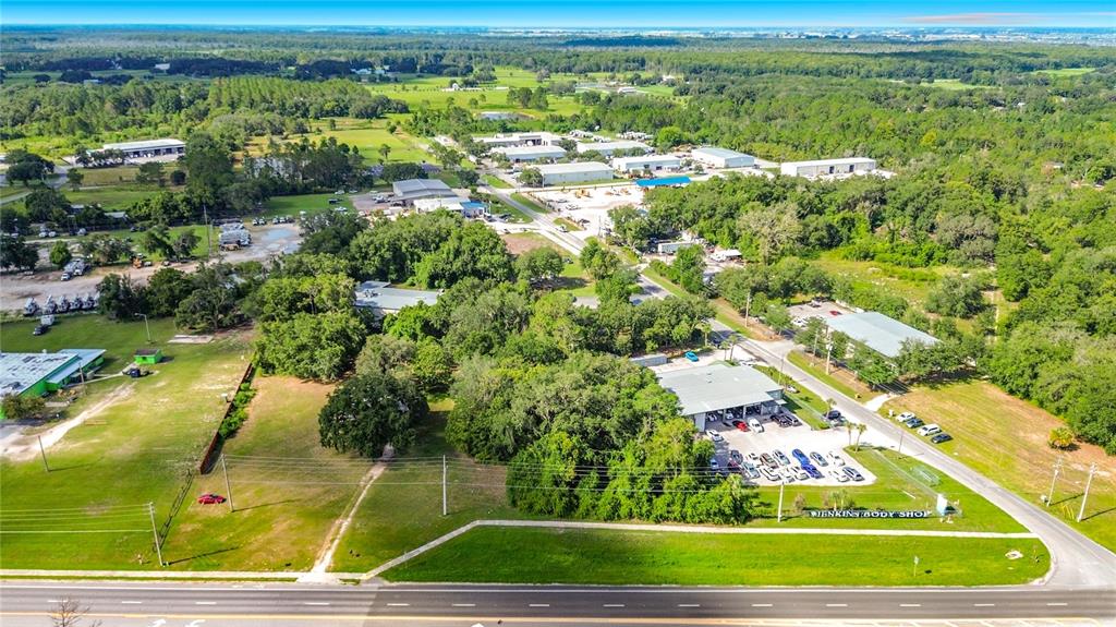 An aerial view shows a commercial property with a body shop and surrounding wooded land — 1450 STATE ROAD 44, LEESBURG, FL