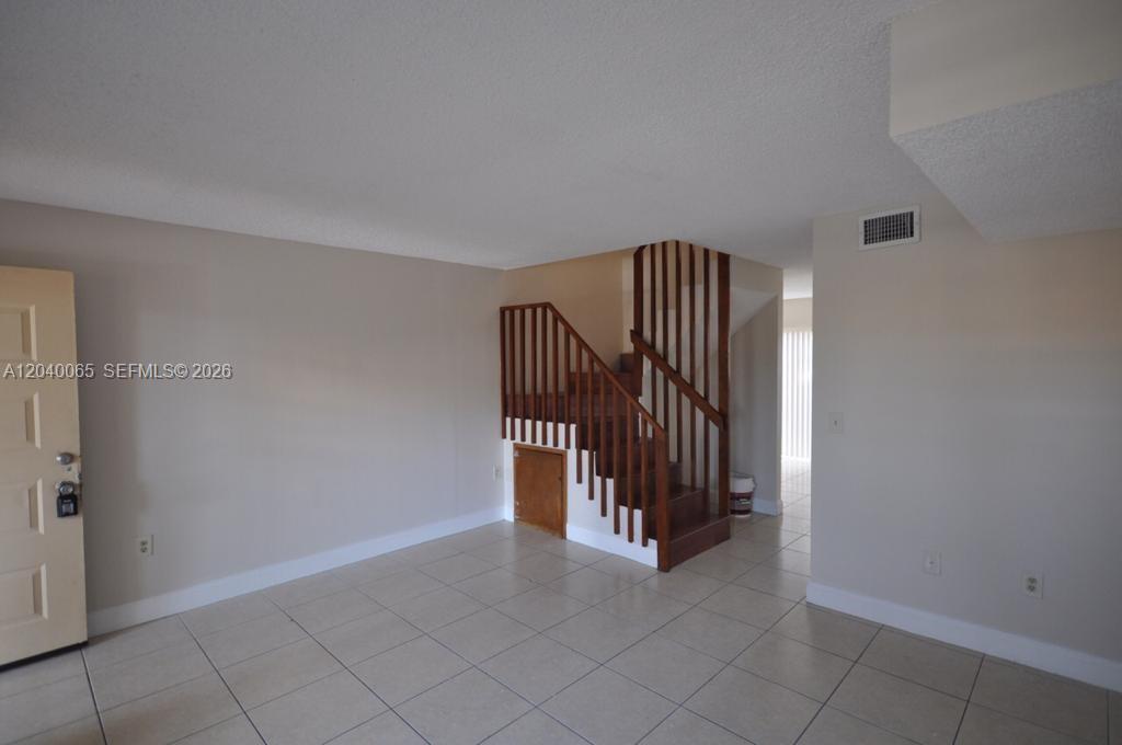 An interior room features light tile flooring, beige walls, and a wooden staircase — MIAMI, FL