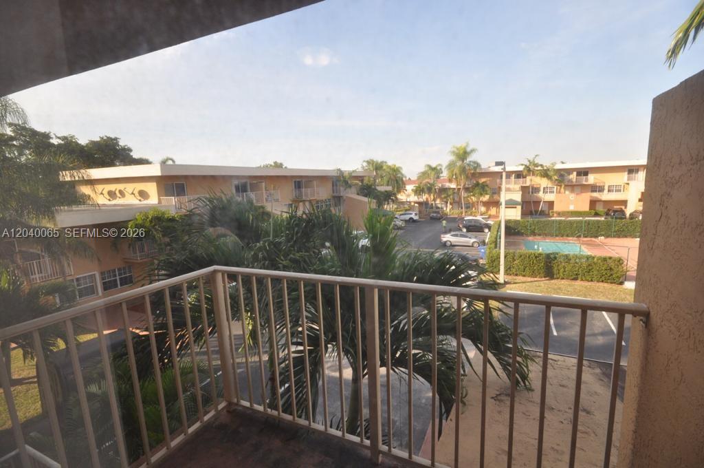 A view from a balcony overlooking a parking lot, palm trees, and apartment buildings — MIAMI, FL