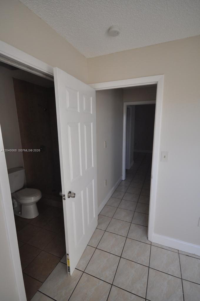 A white door opens to a bathroom with a toilet and tiled flooring — MIAMI, FL