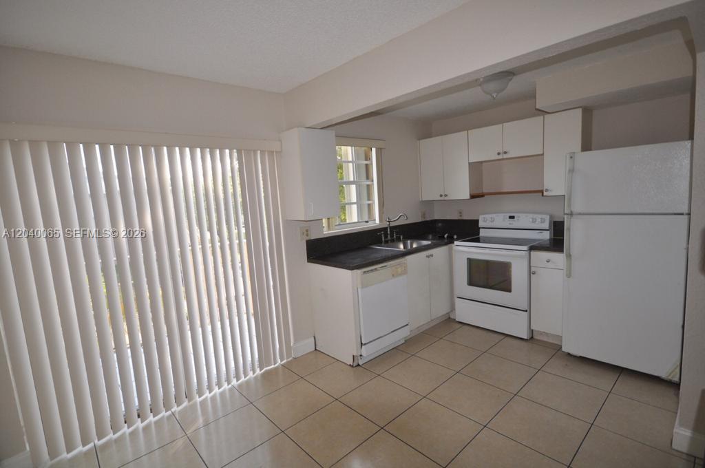 A kitchen features white cabinets, white appliances, dark countertops, and light-colored tile flooring — MIAMI, FL