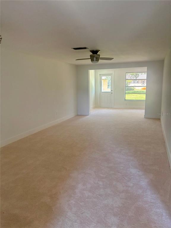 A carpeted living room features a ceiling fan and a doorway leading to the outdoors — 4347 RUSTIC DRIVE, NEW PORT RICHEY, FL