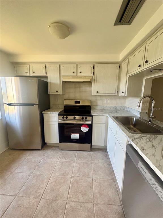 A kitchen features white cabinets, stainless steel appliances, and light-colored tile flooring — 4347 RUSTIC DRIVE, NEW PORT RICHEY, FL