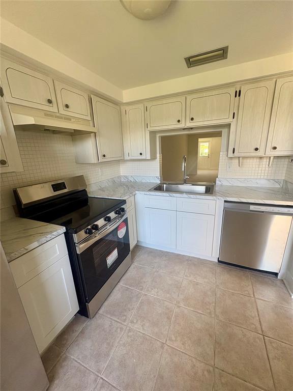 A kitchen features white cabinets, marble-look countertops, stainless steel appliances, and beige tile flooring — 4347 RUSTIC DRIVE, NEW PORT RICHEY, FL