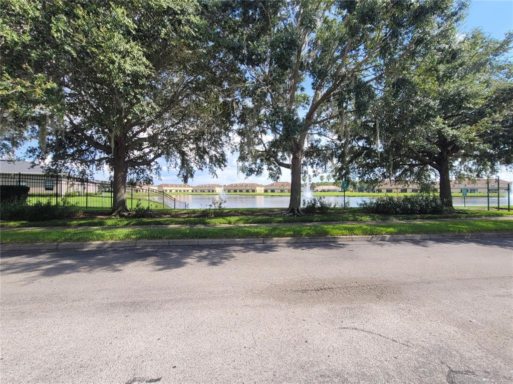 A view of a pond with fountains framed by large trees behind a street — 3321 WHITESTONE CIRCLE UNIT 108, KISSIMMEE, FL